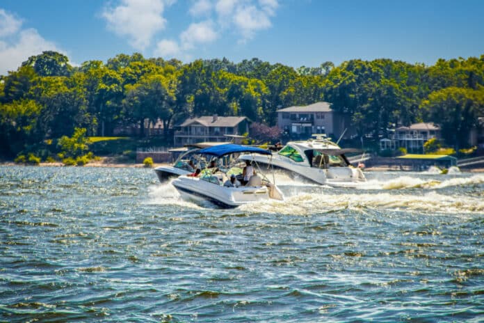 Three speedboats at lake racing in choppy water past lakeside ho