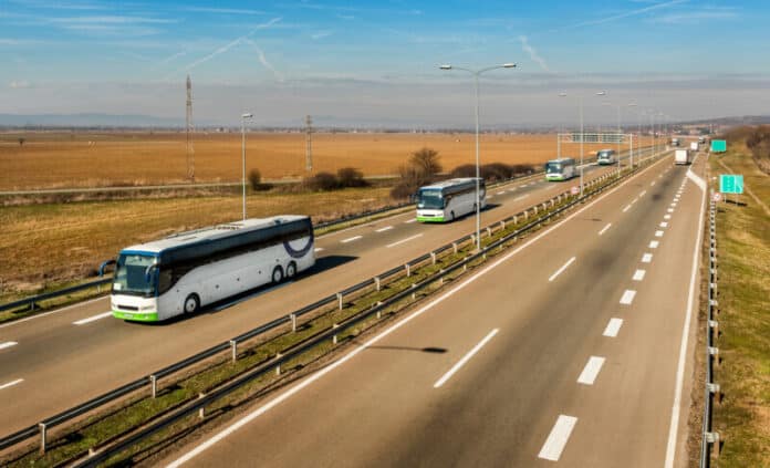 Caravan or convoy of Four white buses in line traveling on a country highway under amazing blue sky. Highway school children transportation with white buses.