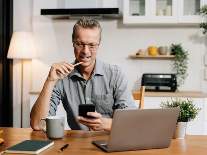 Lifestyle people, using laptop computer and smartphone sitting in the kitchen. Happy mature male, entrepreneur, small business owner working online at home office.